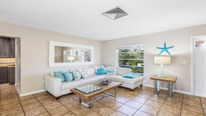 A living room with a white sofa, a coffee table, a starfish decoration, and a window with a view of greenery. - Unwind in Paradise on Marco Island (Marco Island)