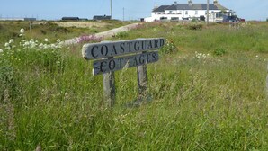 A coastal cottage sign in a grassy field with a white building in the background. - Pass the Keys | Levante Coastal Cabin - Dungeness, Sleeps 2/3 (Folkestone)
