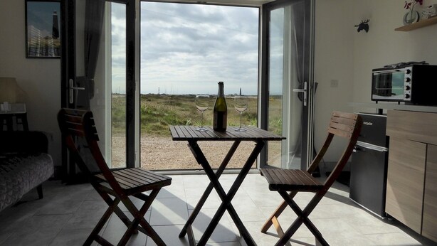 A room with a table and two chairs, a microwave, and a refrigerator. - Pass the Keys | Levante Coastal Cabin - Dungeness, Sleeps 2/3 (Folkestone)