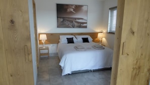 A neatly arranged bedroom with a large bed, two bedside tables with lamps, a wooden headboard, and a painting on the wall. - Pass the Keys | Levante Coastal Cabin - Dungeness, Sleeps 2/3 (Folkestone)