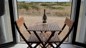 A wooden table and chairs set up on a balcony with a bottle of champagne and glasses on it. - Mistral Coastal Cabin - Dungeness, sleeps 2/3 - Pass the Keys (Folkestone)