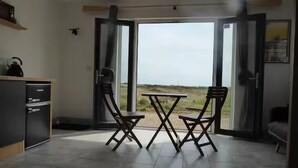 A room with a dining table and chairs, a kitchen area, and a sliding glass door leading to a view. - Mistral Coastal Cabin - Dungeness, sleeps 2/3 - Pass the Keys (Folkestone)