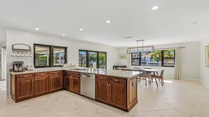 Een moderne keuken met een groot eiland, houten kastjes en uitzicht op de omgeving door grote ramen.