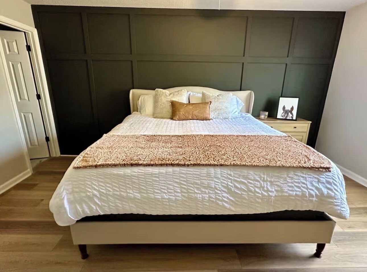 Ein Bett mit gemustertem Überwurf, ein Nachttisch mit Bilderrahmen und ein dunkles Kopfteil.