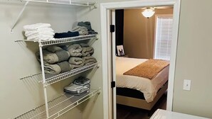 A small bedroom with a bed, a walk-in closet with shelves, and a trash can.