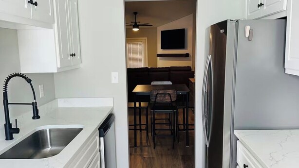 A modern kitchen with white cabinetry, a stainless steel refrigerator, and a wooden floor.