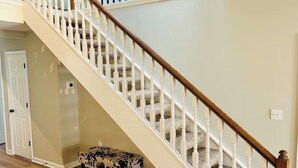 A staircase with white balusters and wooden handrails, carpeted steps, and a bench at the bottom.