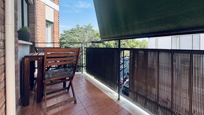 A balcony with a wooden chair and table, a potted plant, and a view of parked cars through a metal fence. - Trastevere Terrace Bright Apartment (Roma)