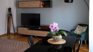 A modern living room with a flat-screen TV, a tripod, a table with a vase of flowers, and a green armchair. - Trastevere Terrace Bright Apartment (Roma)