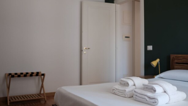 A hotel room with a bed, a wooden chair, a door, and a lamp. - Trastevere Terrace Bright Apartment (Roma)