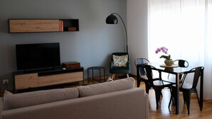 A modern living room with a flat-screen TV, a sofa, a dining table with chairs, a floor lamp, and a small side table. - Trastevere Terrace Bright Apartment (Roma)
