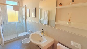 Uma casa de banho moderna com cabine de duche em vidro, lavatório branco e um espelho grande.