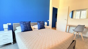 Quarto com cama, duas mesas de cabeceira, uma cadeira, escrivaninha e espelho.