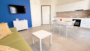 Uma sala de estar moderna com um sofá verde, uma mesa branca e um espaço de jantar com cadeiras brancas.