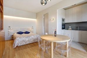 Un dormitorio moderno con cama, mesitas de noche y una pequeña cocina equipada con microondas y hervidor.