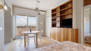 Ein modernes Schlafzimmer mit Bett, Fernseher, einer Holztrennwand und einem Essbereich mit Tisch und Stühlen.