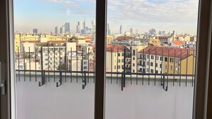 Blick durch ein Fenster mit Metallgitter, einem Backboden und einer Stadtansicht im Hintergrund.