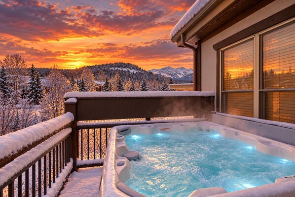 A hot tub with a view of snow-covered trees and mountains during sunset.