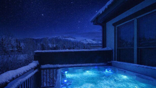 Ein Whirlpool mit Blick auf einen sternenklaren Nachthimmel, umgeben von schneebedeckten Bäumen und einem Berg im Hintergrund.