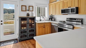 A modern kitchen with wooden cabinets, a built-in microwave, a stove, and a coffee maker. There's a window with a view of a forest. - Family Ski Loft at Kristi – Walk to Chair 8, Game Room, Views (Brian Head)
