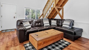 A modern living room with a wooden staircase, a leather sectional sofa, and a wooden coffee table. - Family Ski Loft at Kristi – Walk to Chair 8, Game Room, Views (Brian Head)