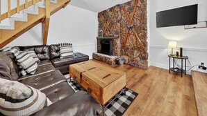 A modern living room with a leather sofa, a wooden coffee table, a stone fireplace, and a TV mounted on the wall. - Family Ski Loft at Kristi – Walk to Chair 8, Game Room, Views (Brian Head)