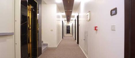 A long, narrow hallway with doors on both sides, carpeted floor, and a ceiling with recessed lighting.
