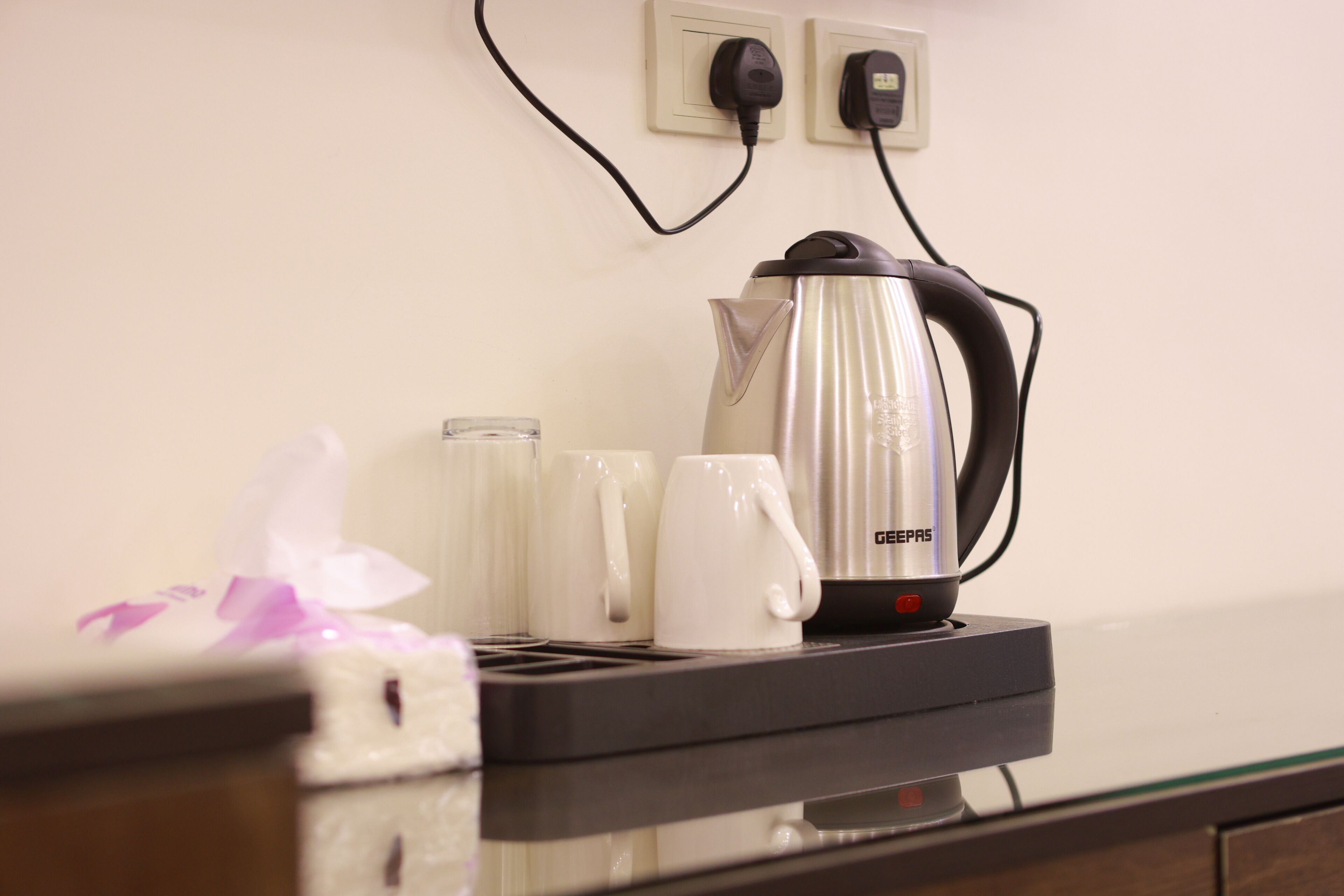 A kitchen area with a GEPEPS electric kettle, a toaster, and two white mugs on a glass countertop.