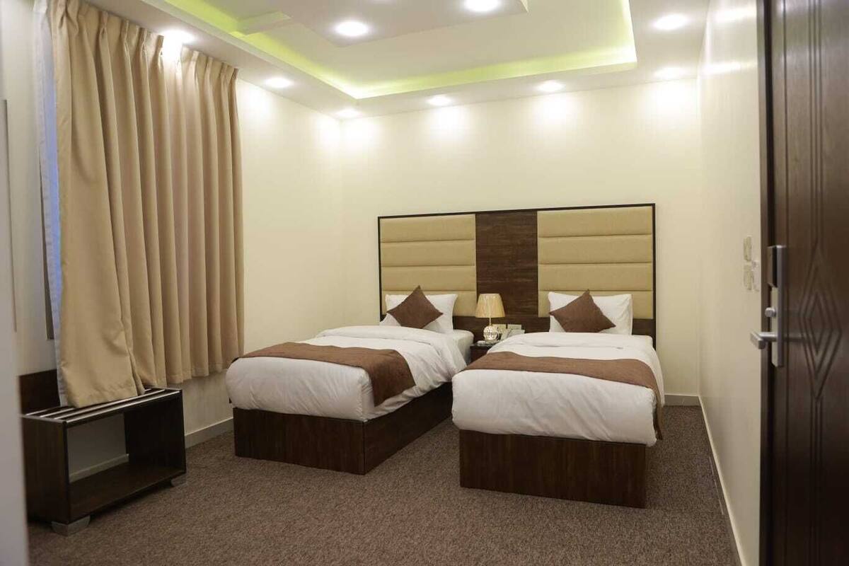 A hotel room with two beds, a nightstand, a lamp, and a wooden wardrobe.