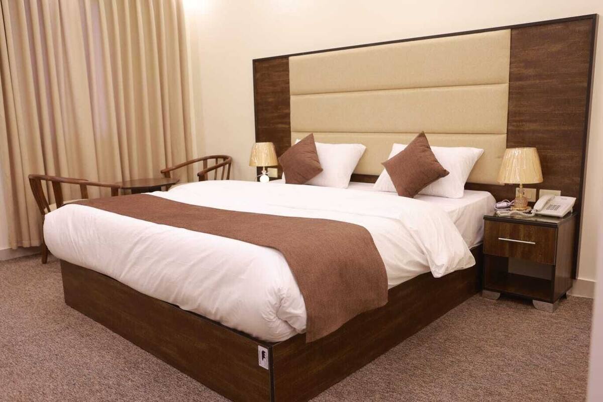 A hotel room with a large bed, two bedside tables, a chair, and a lamp.