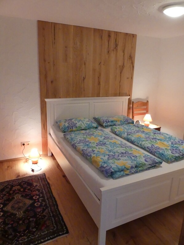 A bedroom with a wooden headboard, a bed with floral bedding, two bedside lamps, and a patterned rug.
