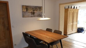 Un coin repas avec une table en bois et quatre chaises, un luminaire suspendu et un tableau représentant un cerf accroché au mur.