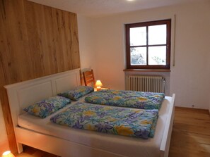 A bedroom with a wooden headboard, a window with a view, a radiator, and a bedside lamp.