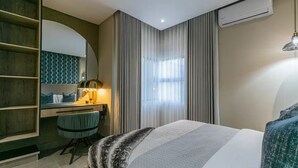 Habitación de hotel con cama, escritorio, silla, espejo y ventana con cortinas.