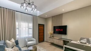 Una sala de estar moderna con un sofá, un sillón, una mesa de centro, un televisor montado en la pared y un mueble de madera.