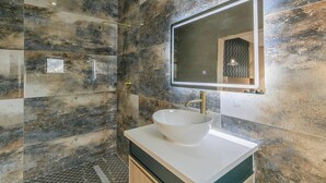 Un baño moderno con un espejo grande, un lavabo tipo recipiente y una zona de ducha.