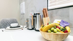 Una escena de desayuno con una cesta de frutas, una cafetera y un tostador sobre una mesa.