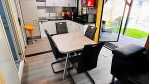 A modern kitchen with white cabinets, a dining table with chairs, a red microwave, and a large window. - Tiny House 200 with Private Terrace, Garden, and Wi-Fi (Zadelsdorf)