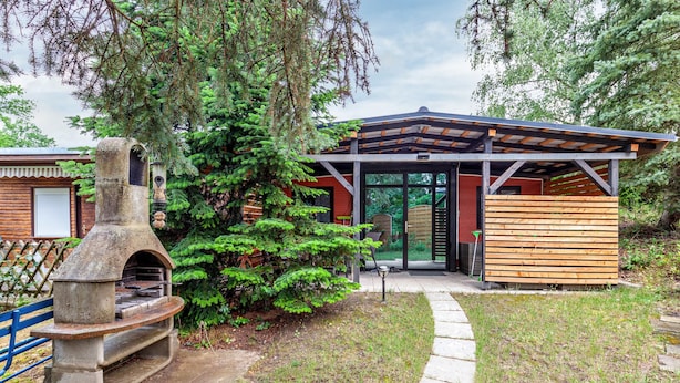 A rustic outdoor kitchen with a stone oven, a wooden pergola, and a wooden structure with glass doors. - Tiny House 200 with Private Terrace, Garden, and Wi-Fi (Zadelsdorf)