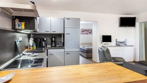 A compact kitchen with a stove, coffee maker, and cabinets, a dining area with a table and chairs, a bed, and a TV in a separate room. - Holiday Apartment "Zum Segel" 2 with Private Terrace and Wi-Fi (Zadelsdorf)