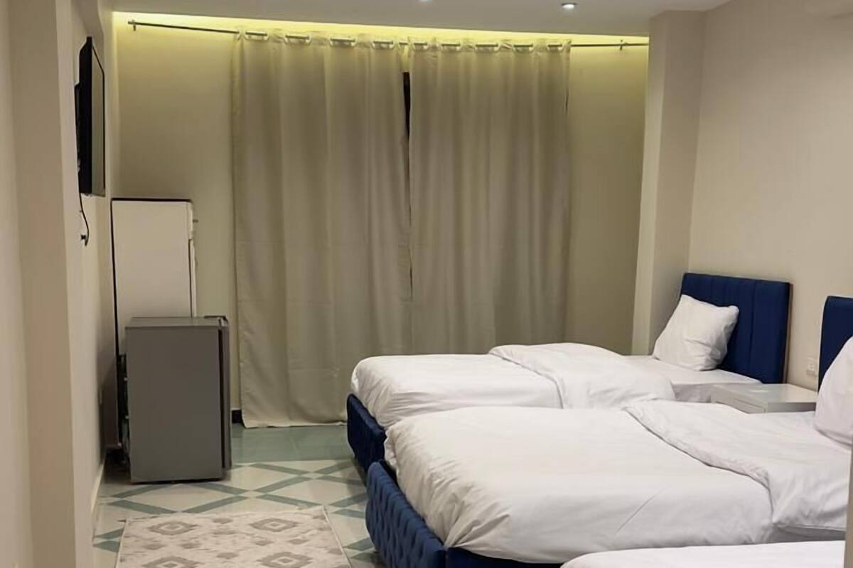 A hotel room with two beds, a small refrigerator, and a patterned rug.