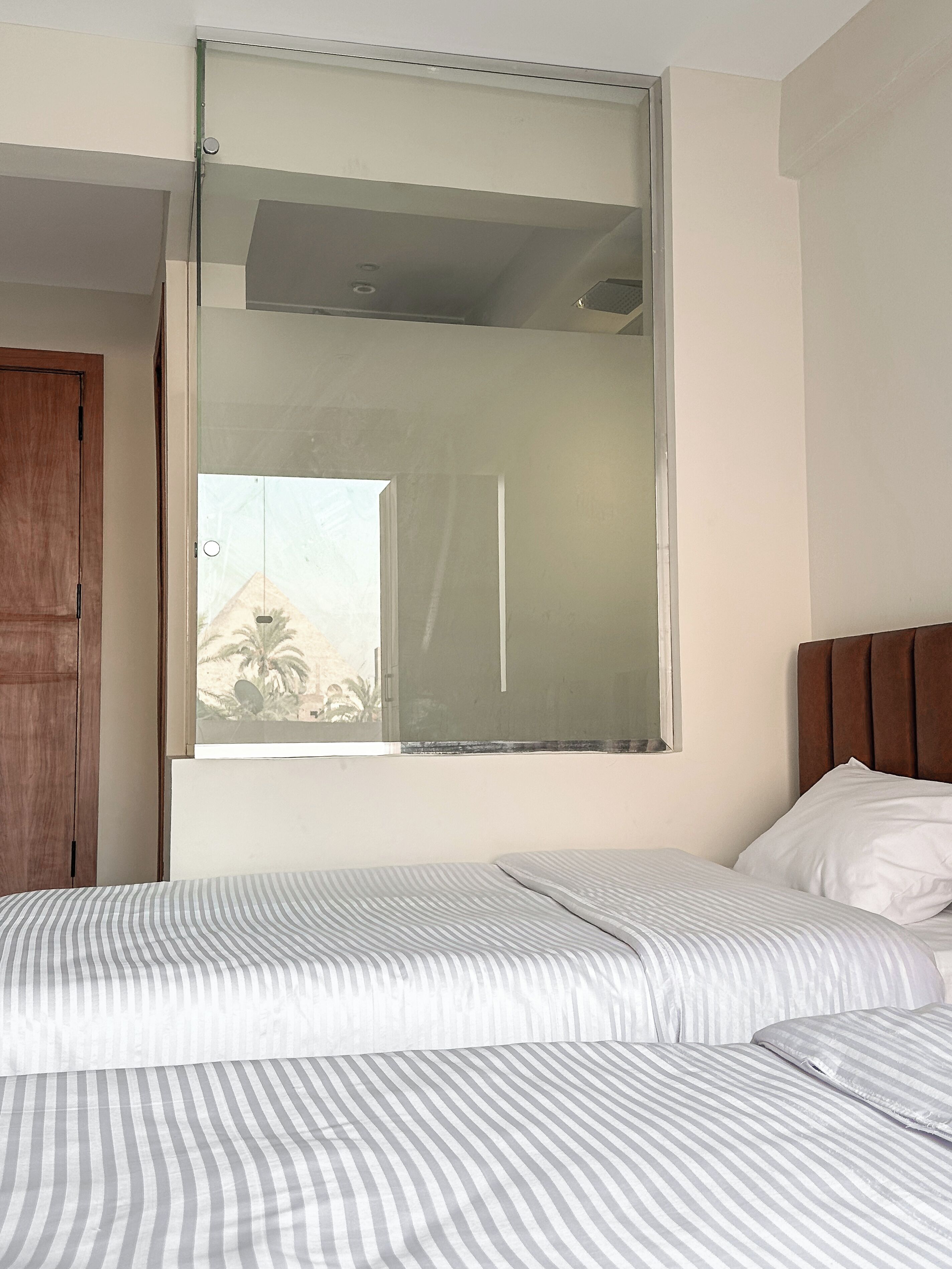 Habitación de hotel con cama, armario de madera y ventana grande con vista a palmeras.