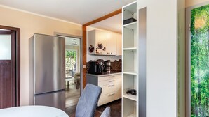 Een moderne keuken met een roestvrijstalen koelkast, een koffiezetapparaat, en een eethoek met een witte tafel en een grijze stoel.