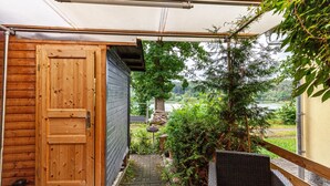 Een houten deur, een overdekt terras met uitzicht op een meer, en een rieten stoel.