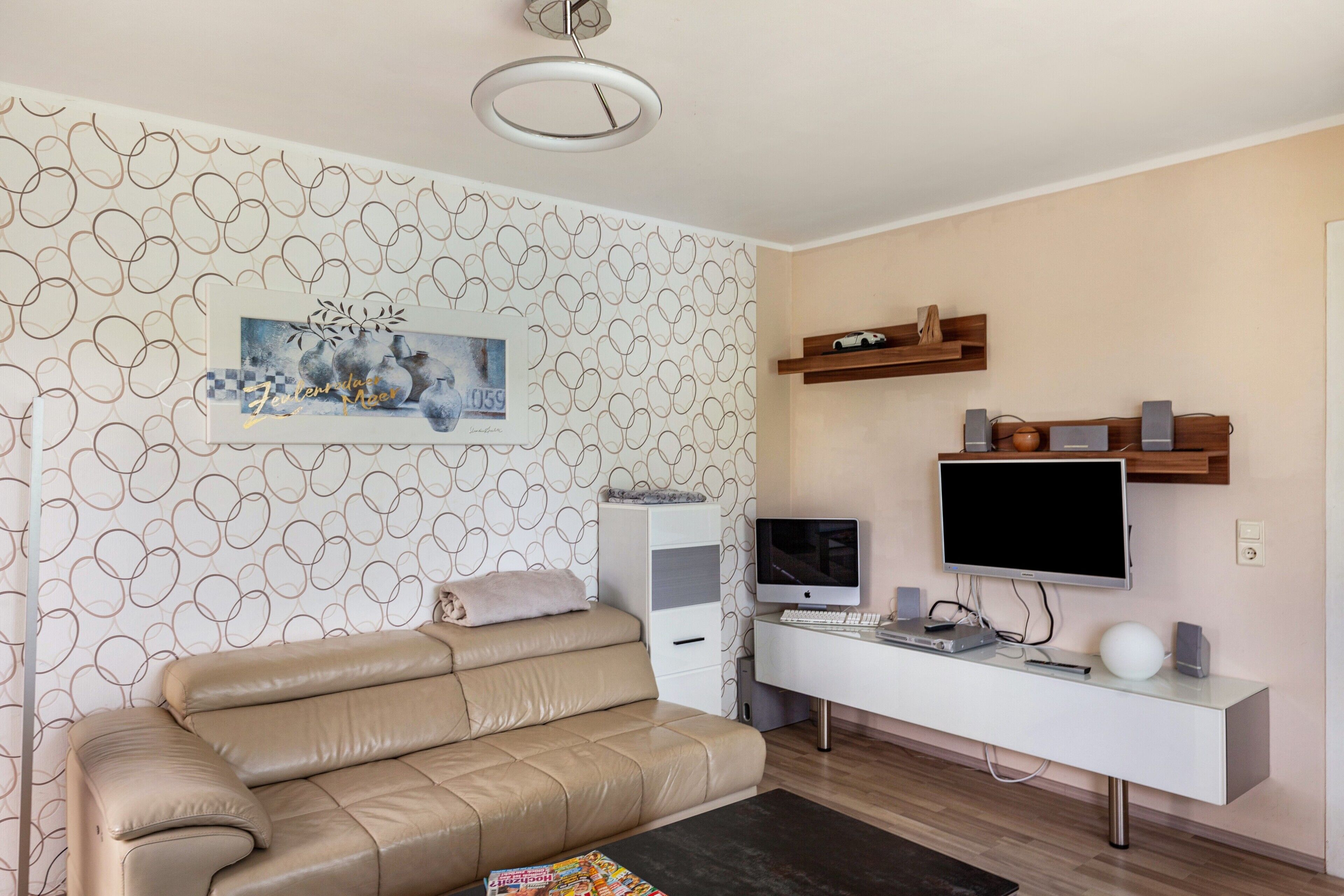 Un soggiorno moderno con un divano, una TV a schermo piatto, una scrivania con un computer e una parete decorata con un motivo circolare.