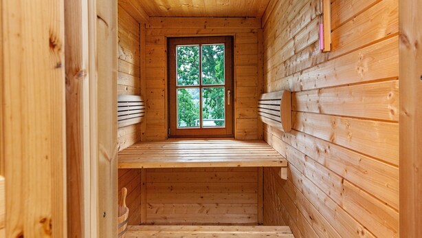 Een houten hut van binnen met een raam, houten wanden en een bankje.