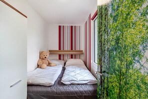 A small, compact room with two beds, a teddy bear, and a window with a view of trees. - Holiday Home 257 with Lake View, Private Terrace, and Wi-Fi (Zadelsdorf)