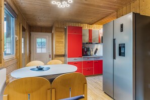 Une cuisine moderne avec des murs en bois, un réfrigérateur en acier inoxydable, des armoires rouges et un coin repas avec une table blanche et des chaises en bois.