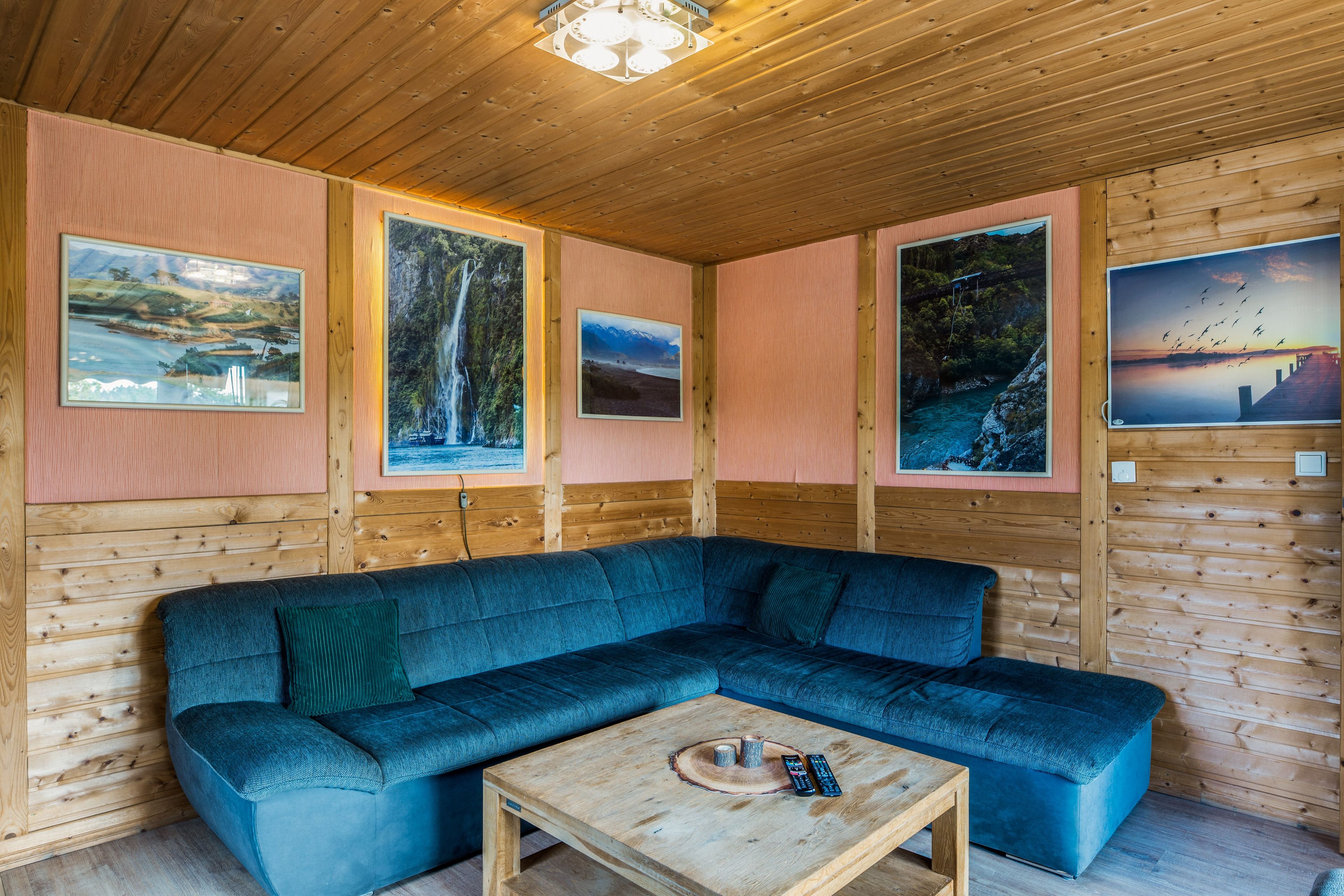Een gezellige kamer met een blauwe hoekbank, houten wanden en landschaptaferelen in lijsten.