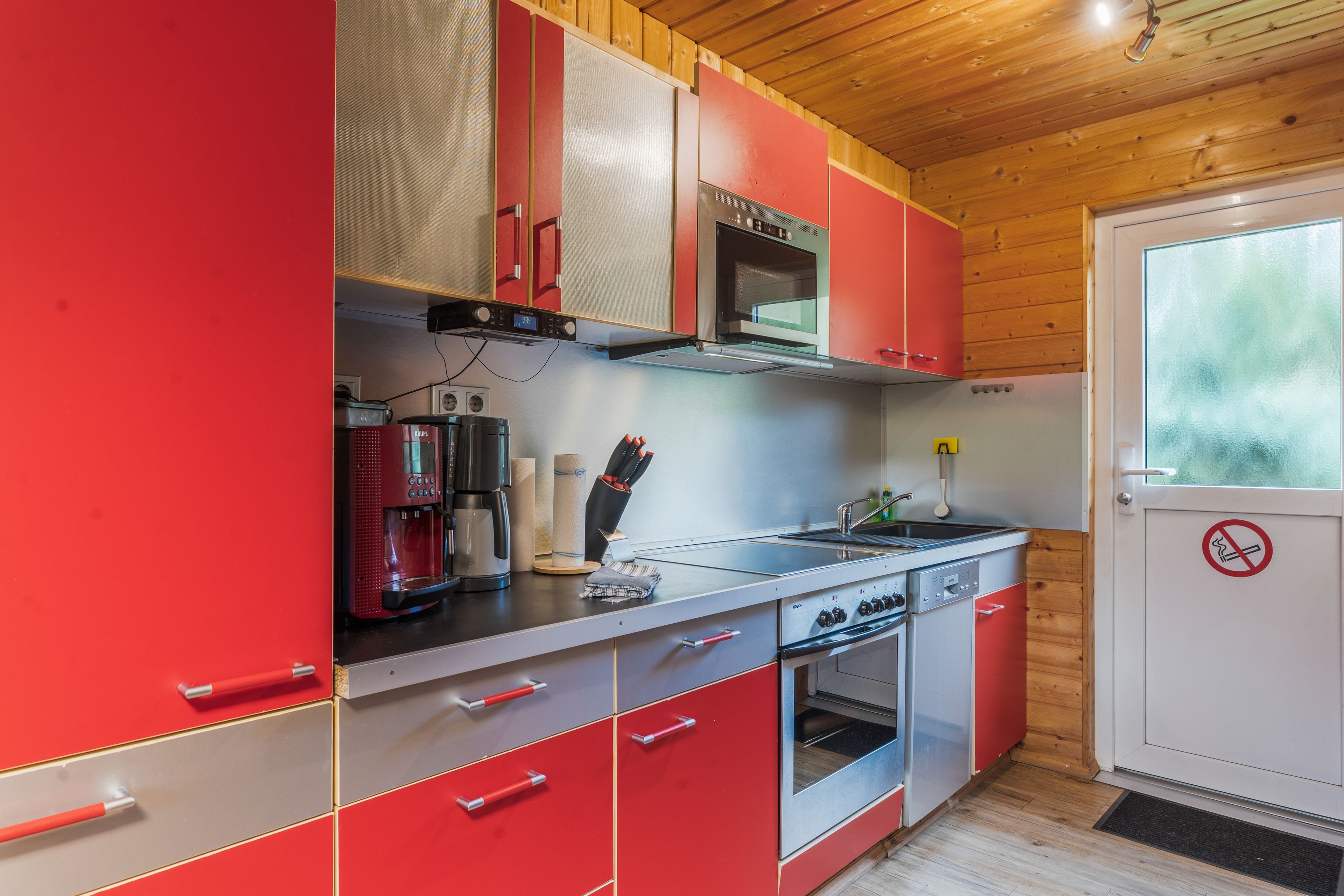 A kitchen with red cabinets, a Bosch oven, a coffee maker, and a microwave.